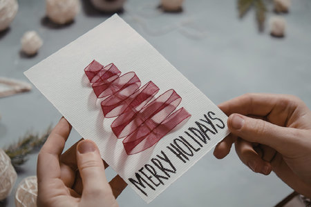 A person holding a white Christmas card with a red tree and 'Merry Holidays' written on itの写真素材