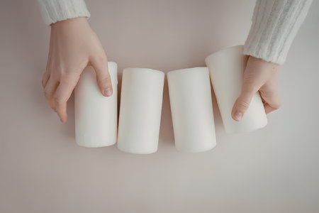 A pair of hands holding four white cylindrical objects on a pink backgroundの写真素材