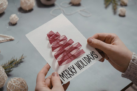 A person holding a holiday card with a Christmas tree and the words 'Merry Holidays' written on itの写真素材