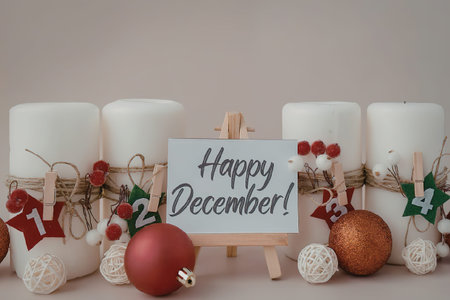 A festive arrangement of white candles, Christmas ornaments, and a sign that reads 'Happy December!' on a small wooden easel.の写真素材