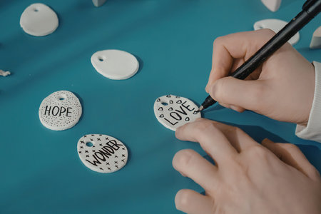 A person painting small stones with inspirational words like 'HOPE', 'LOVE', and 'HOME'.の写真素材