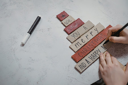 A person painting Christmas wooden tiles with a marker, creating a merry and happy holiday...