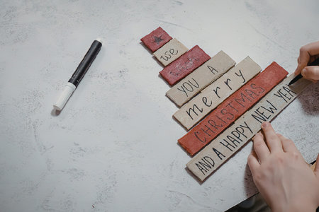 A person's hands painting Christmas tiles with a marker on a white surface.