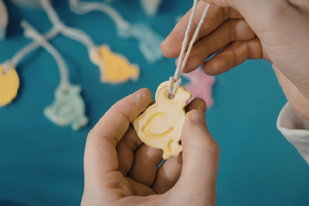 A person is threading a yellow Easter egg shaped decoration with a string.