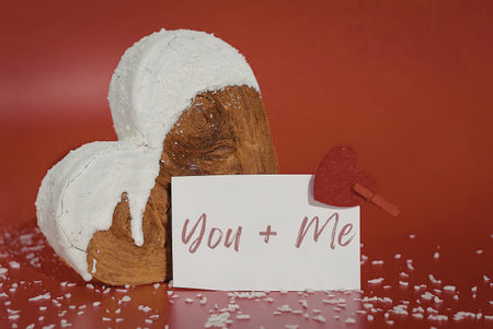 A heart shaped pastry with white icing and a note that says 'You + Me' on a red background with...