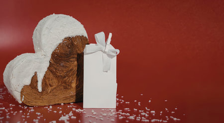 A heart-shaped cake with white frosting and a gift box on a red backgroundの写真素材