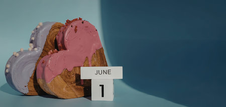 Three heart-shaped donuts with pink and purple frosting next to a calendar marking June 1stの写真素材