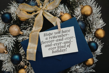 A blue card with a holiday message surrounded by a Christmas wreath with gold, blue, and bronze ornaments and a gold ribbon.の写真素材