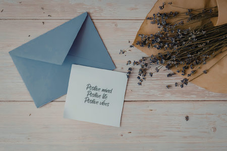 A blue envelope and a white card with black writing on a wooden table with dried lavender flowers