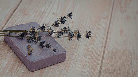 A purple soap bar with a sprig of fresh lavender flowers on top, placed on a light wooden surface.の写真素材