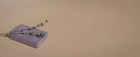 A purple soap bar with dried lavender flowers on top, placed on a beige backgroundの写真素材