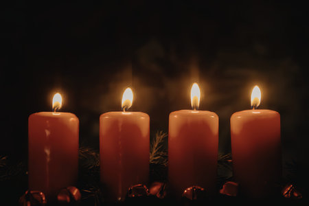 A close-up photograph of four red candles with bright flames burning against a dark background.の写真素材