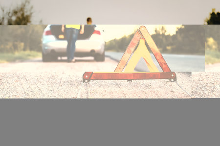 a man in a yellow vest stands behind a silver car with its trunk open on a road, with an orange...