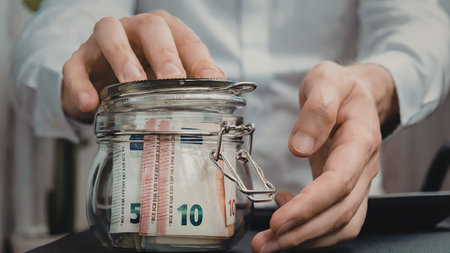 A man in a white shirt putting money into a glass jar