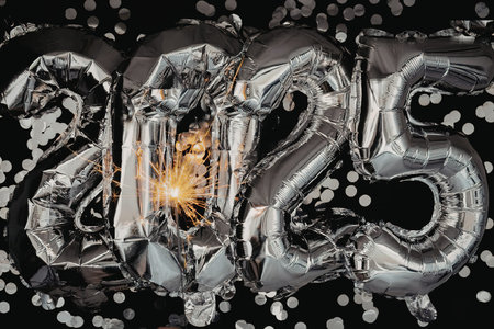 A shiny silver balloon in the shape of 2025 surrounded by confetti on a black backgroundの写真素材
