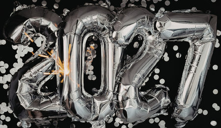 A close-up of silver balloons spelling out 2027, surrounded by confetti on a black background,...