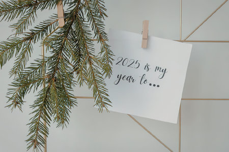 A white card with a note about new year resolutions hanging on a clothespin with a pine tree branch,...