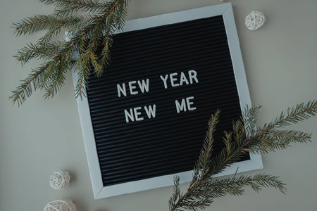 A black letter board with white frame and text 'New Year New Me' surrounded by greenery and white...