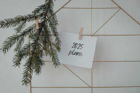 A white card with '2025 plans' written on it, hanging from a clothespin on a geometric gold wire...
