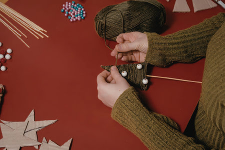 a person wearing a green sweater is crafting with beads and wooden shapes on a red surface