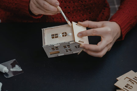 A person in a red sweater is assembling a small wooden house using a tool.の写真素材