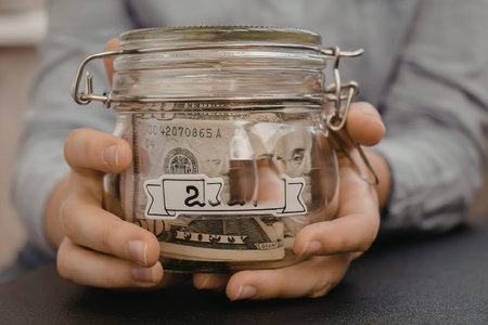 A person holding a glass jar filled with money and labeled 2024.の写真素材