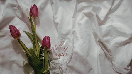 A bouquet of pink tulips in a clear glass vase placed on a crumpled white fabric backgroundの写真素材