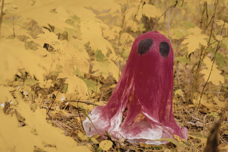 A pink ghost with black eyes sits in a pile of autumn leaves.の写真素材