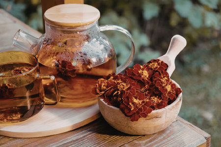 A serene setup featuring a glass teapot with saffron tea, a cup, and a bowl of dried flowers on a...