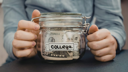 A person holding a jar labeled 'college' filled with moneyの写真素材