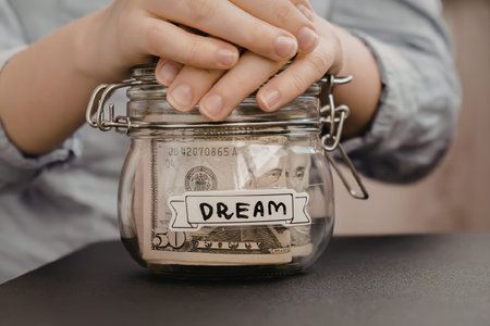 A person saving money in a jar labeled 'dream' on a table.