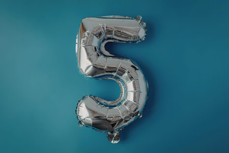 A shiny silver balloon in the shape of the number five against a blue background.の写真素材