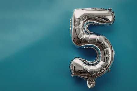 A shiny silver balloon in the shape of the number 5 on a blue background.の写真素材
