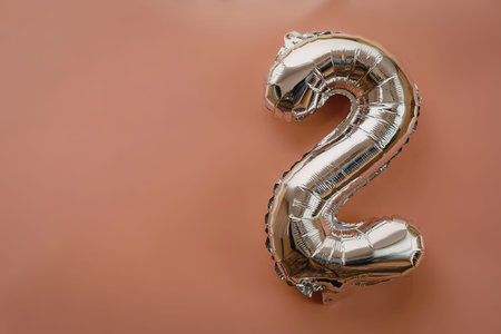 A shiny silver number 2 balloon on a salmon-colored background
