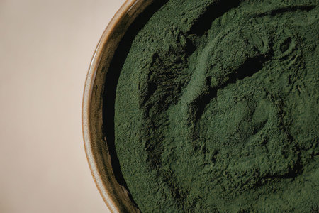 A close-up view of a bowl filled with spirulina powder, showcasing its vibrant green color and...