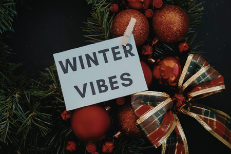 A festive Christmas decoration with red ornaments, green pine branches, and a colorful bow, evoking winter vibes.の写真素材