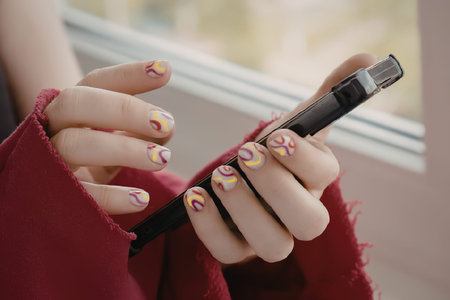 A woman's hands holding a smartphone with colorful nailsの写真素材