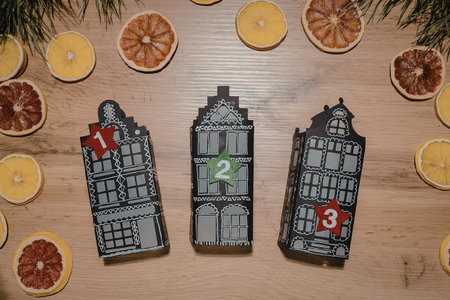 Three grey building-shaped objects on a wooden table surrounded by dried orange and blood orange...