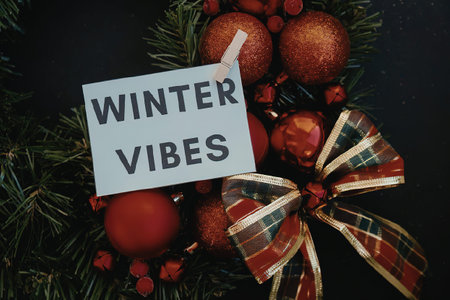 A festive Christmas decoration with red ornaments, green pine branches, and a plaid bow, evoking winter vibes.の写真素材