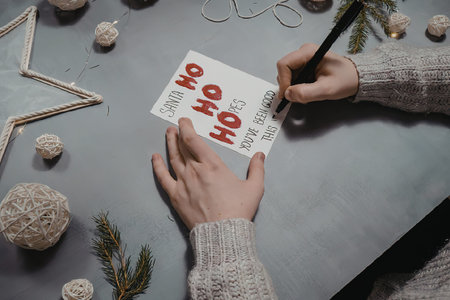 A person's hands writing a Christmas card on a decorated table