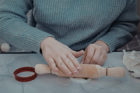 A woman in a blue sweater rolling dough with a wooden rolling pin on a floured surface.
