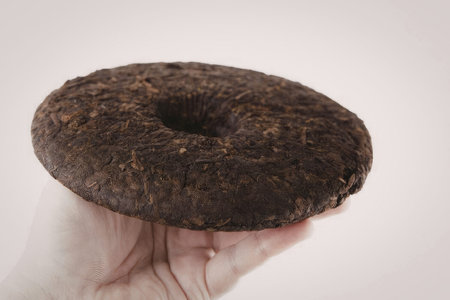 A hand holding a dark brown donut with a hole in the center, likely a chocolate cake donut.