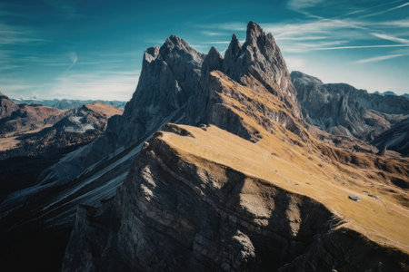 A rugged mountain peak under a clear blue sky with wispy clouds, showcasing rocky terrain and golden...