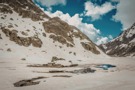 A serene mountainous landscape with snow-covered slopes, a small lake, and a clear blue sky with...