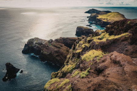 A tranquil coastal scene featuring rugged rocky outcrops covered in greenery, jutting out into the...