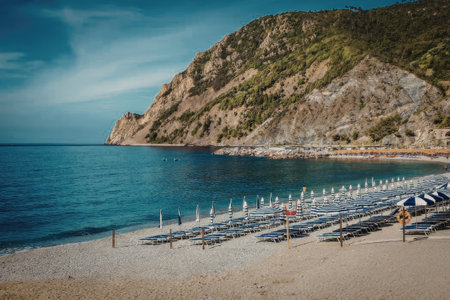 A tranquil beach scene featuring rows of blue chairs on the sandy shore, with a large rocky cliff...
