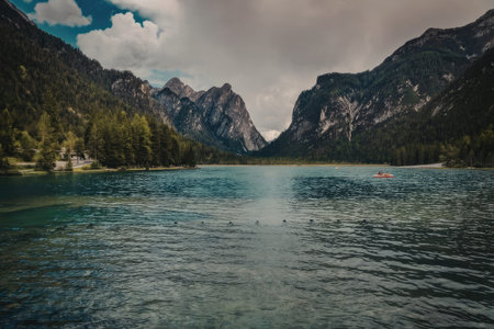 a serene lake with clear water surrounded by mountains and trees under a cloudy skyの写真素材