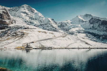 A serene landscape of a snow-covered mountain range reflected in the calm waters of a lake, with a...