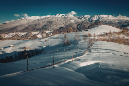 A serene snowy landscape with a fence in the foreground and snow-capped mountains in the background...