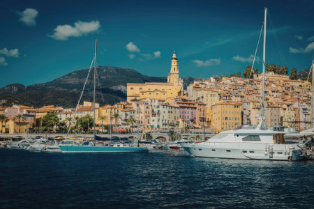 A serene marina scene with boats docked in the water, surrounded by colorful buildings and a mountain in the background under a blue sky with a few clouds.の写真素材